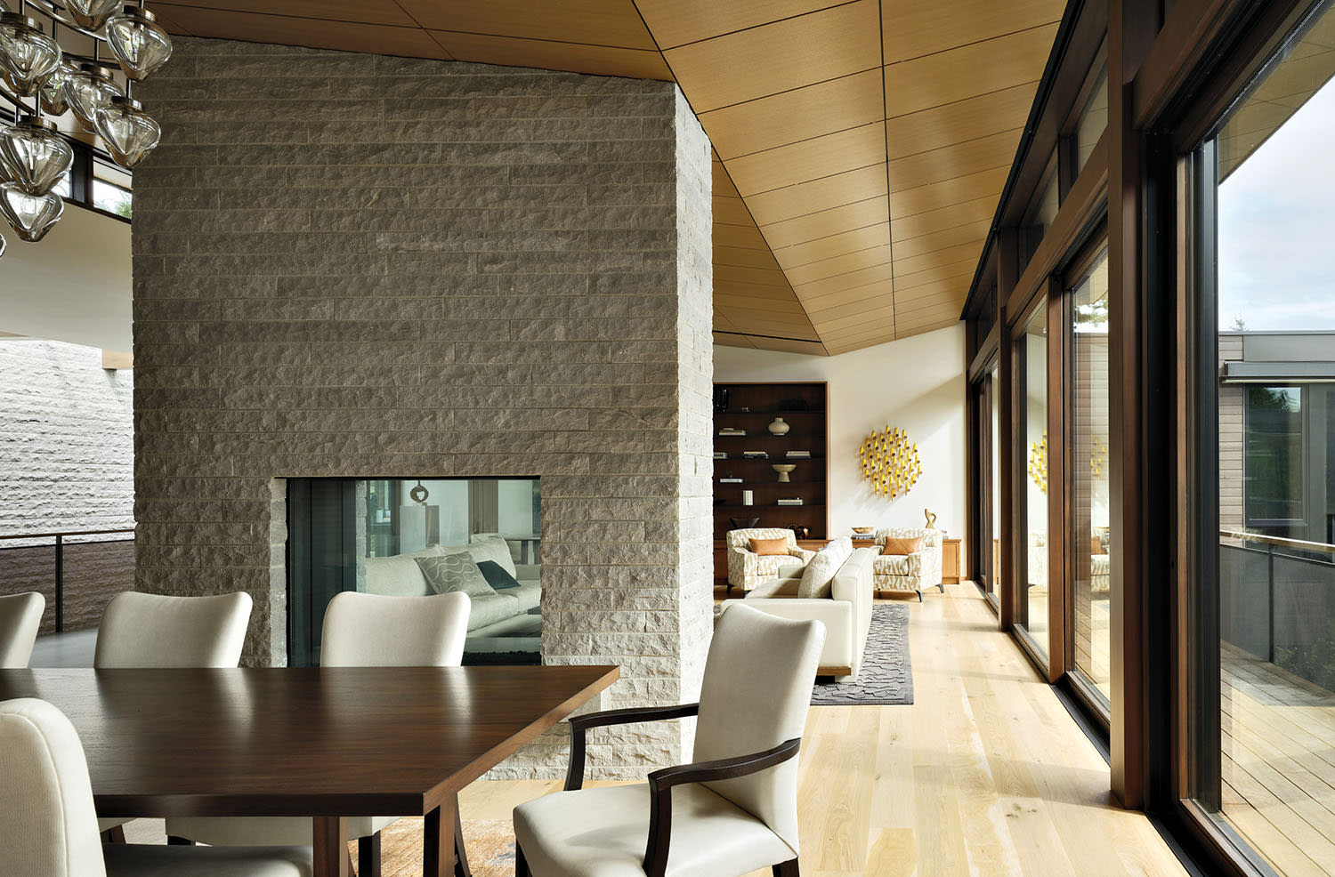 a limestone fireplace separates a living and dining room in a modern home