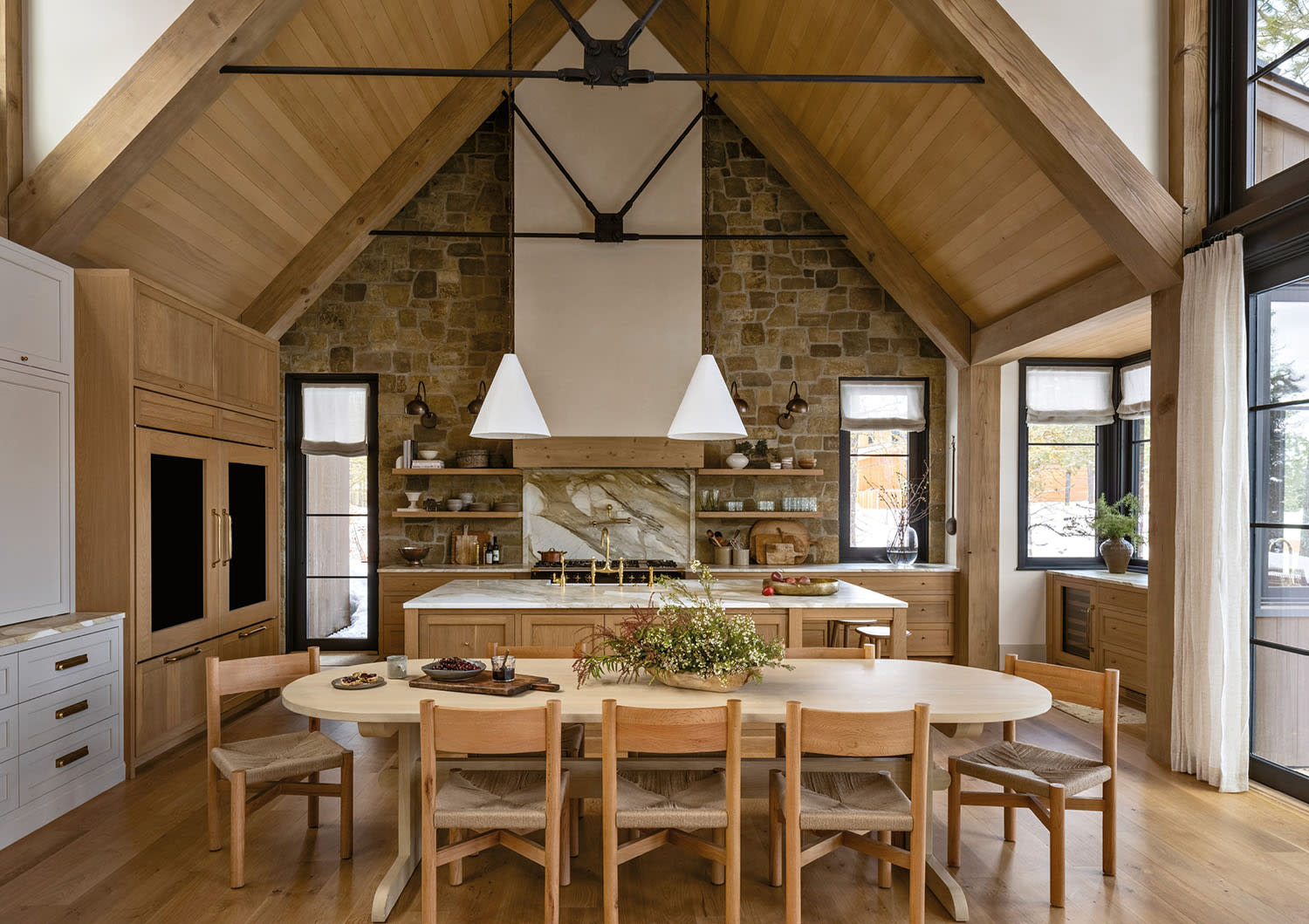 Spacious kitchen and dining room with high vaulted wooden ceiling, stone wall, and large windows