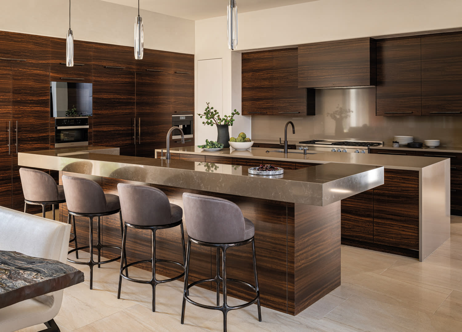Modern kitchen with sleek dark wood cabinets, a polished stone island, and four gray upholstered stools. 