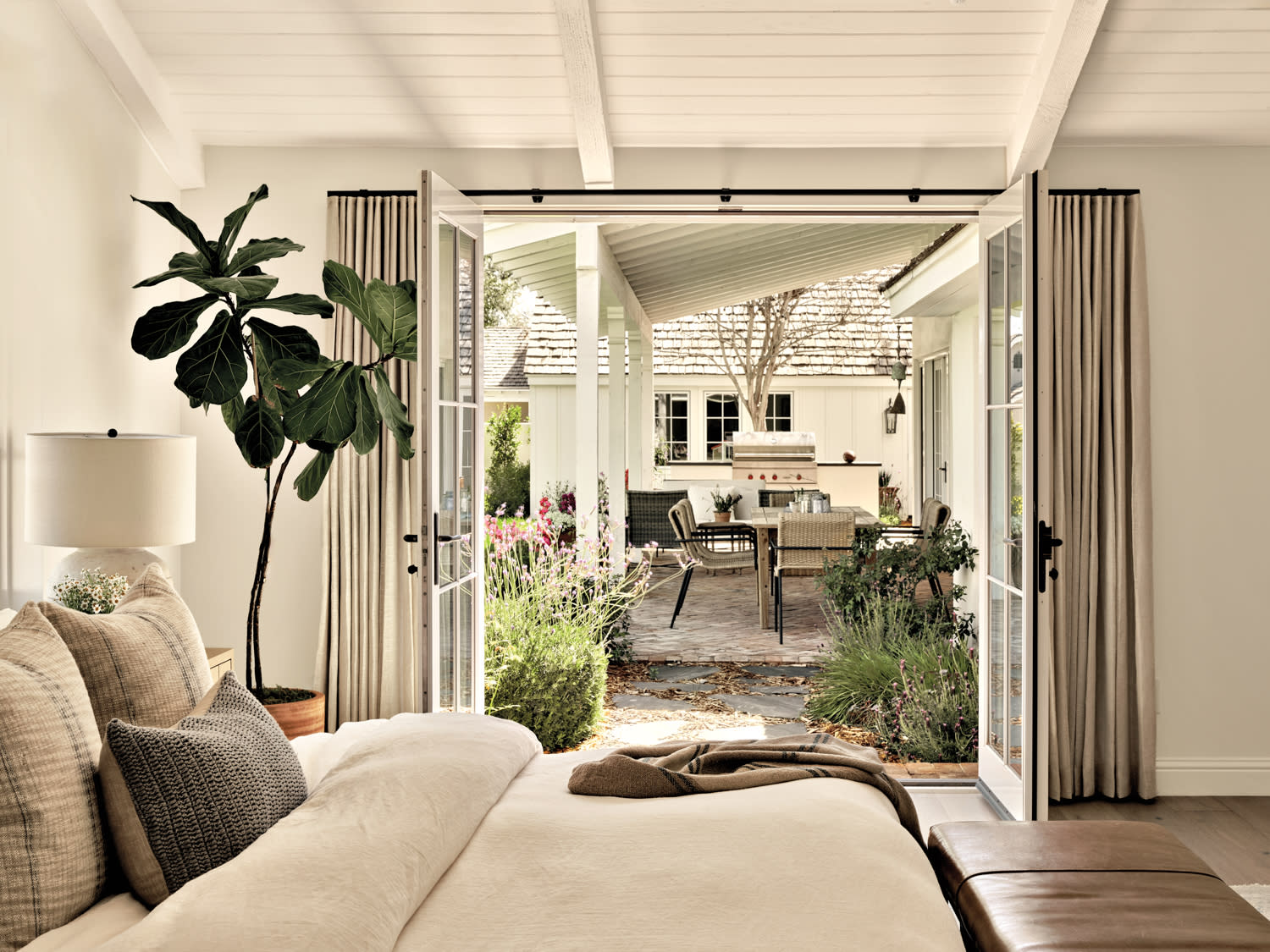 Primary bedroom covered in white and gray linens, which opens to the dining area of a patio