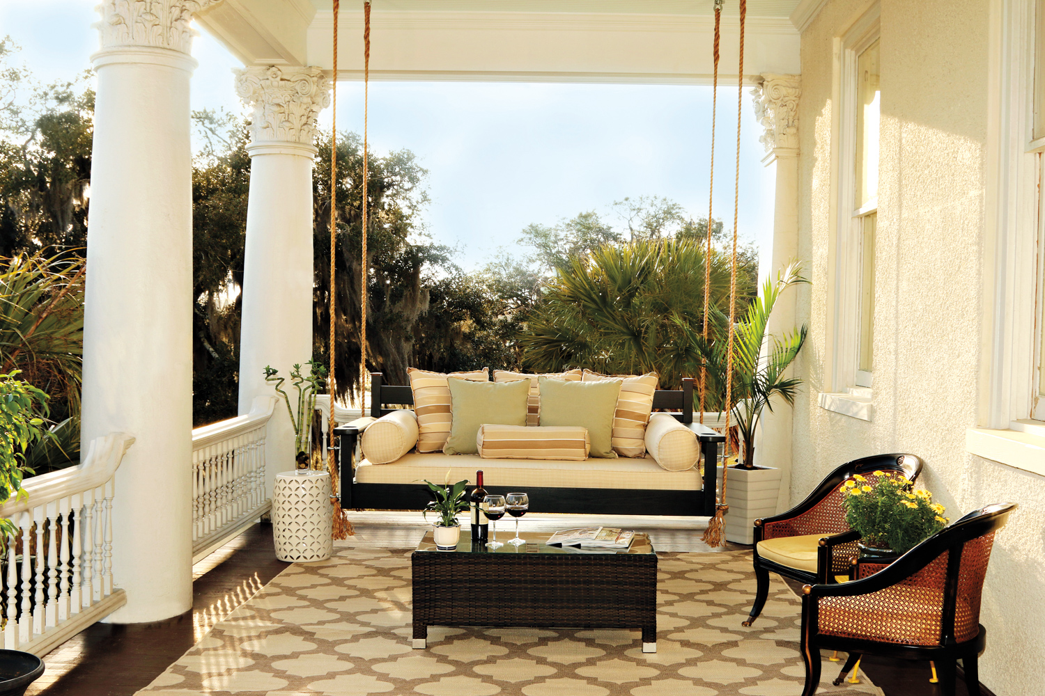 Covered porch with large white columns and sofa swing hanging from the ceiling with coffee table and 2 side chairs