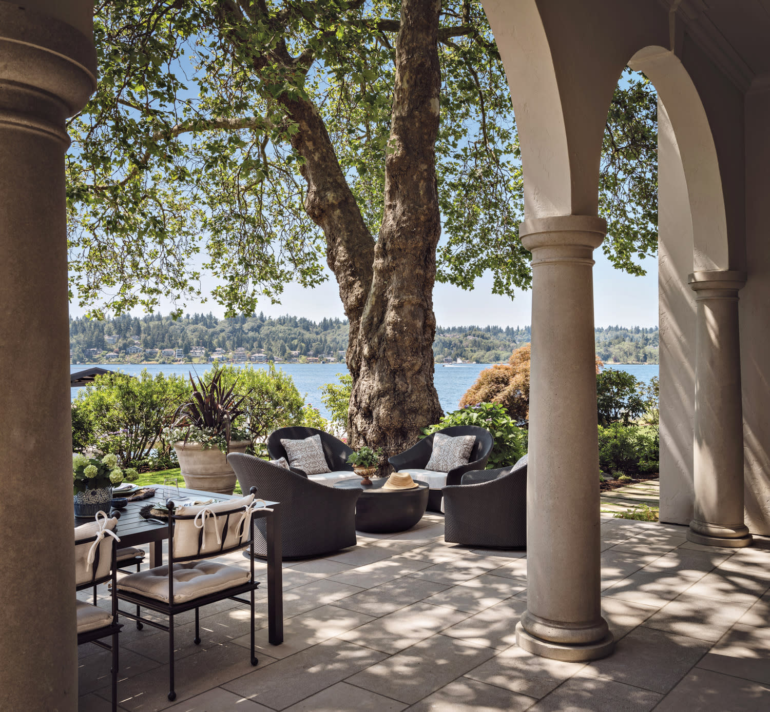 terrace with architectural arches and outdoor seating flanked by a stately tree 