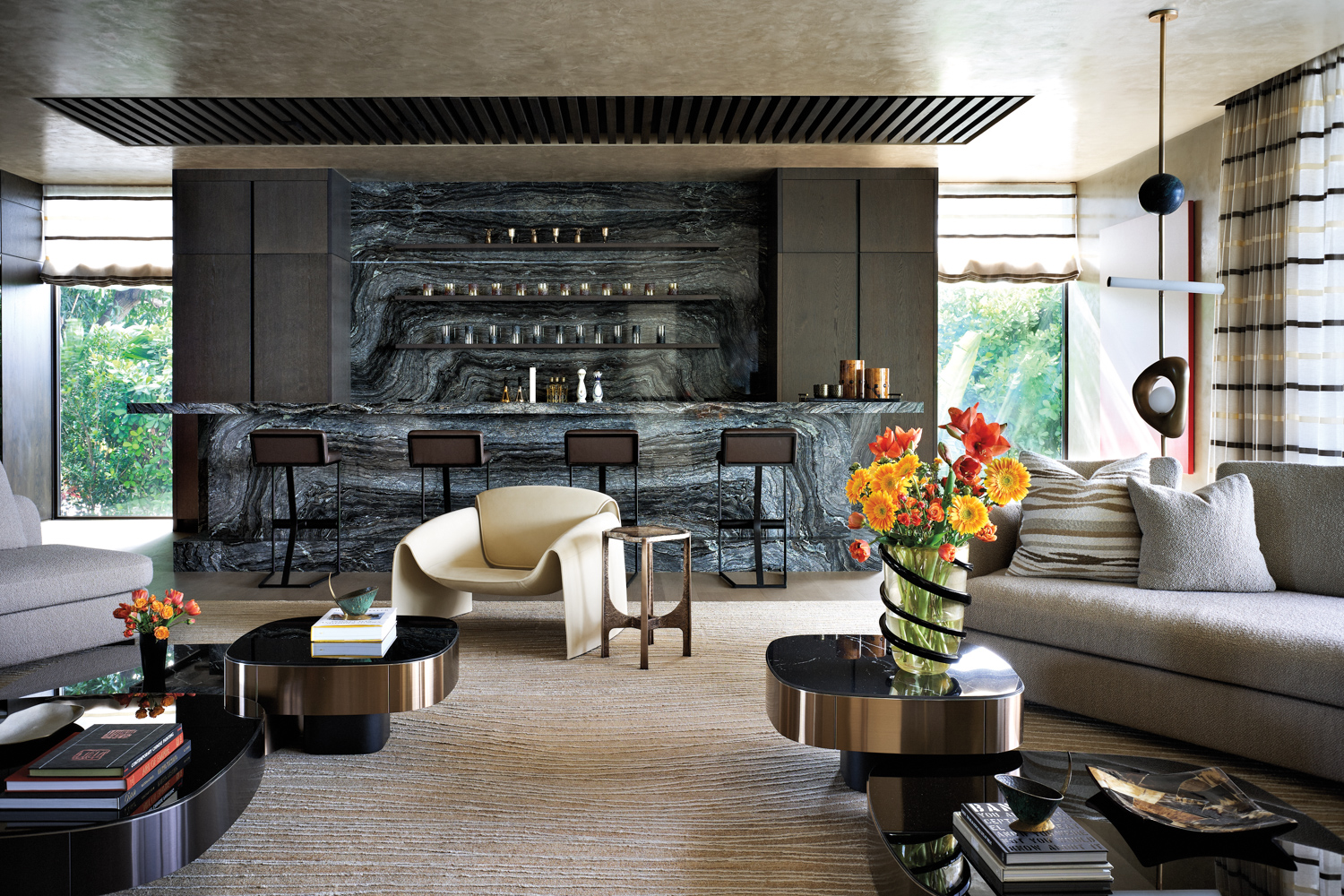 living room with dark marble bar, gray sectional, cream-colored chair and geometric coffee tables