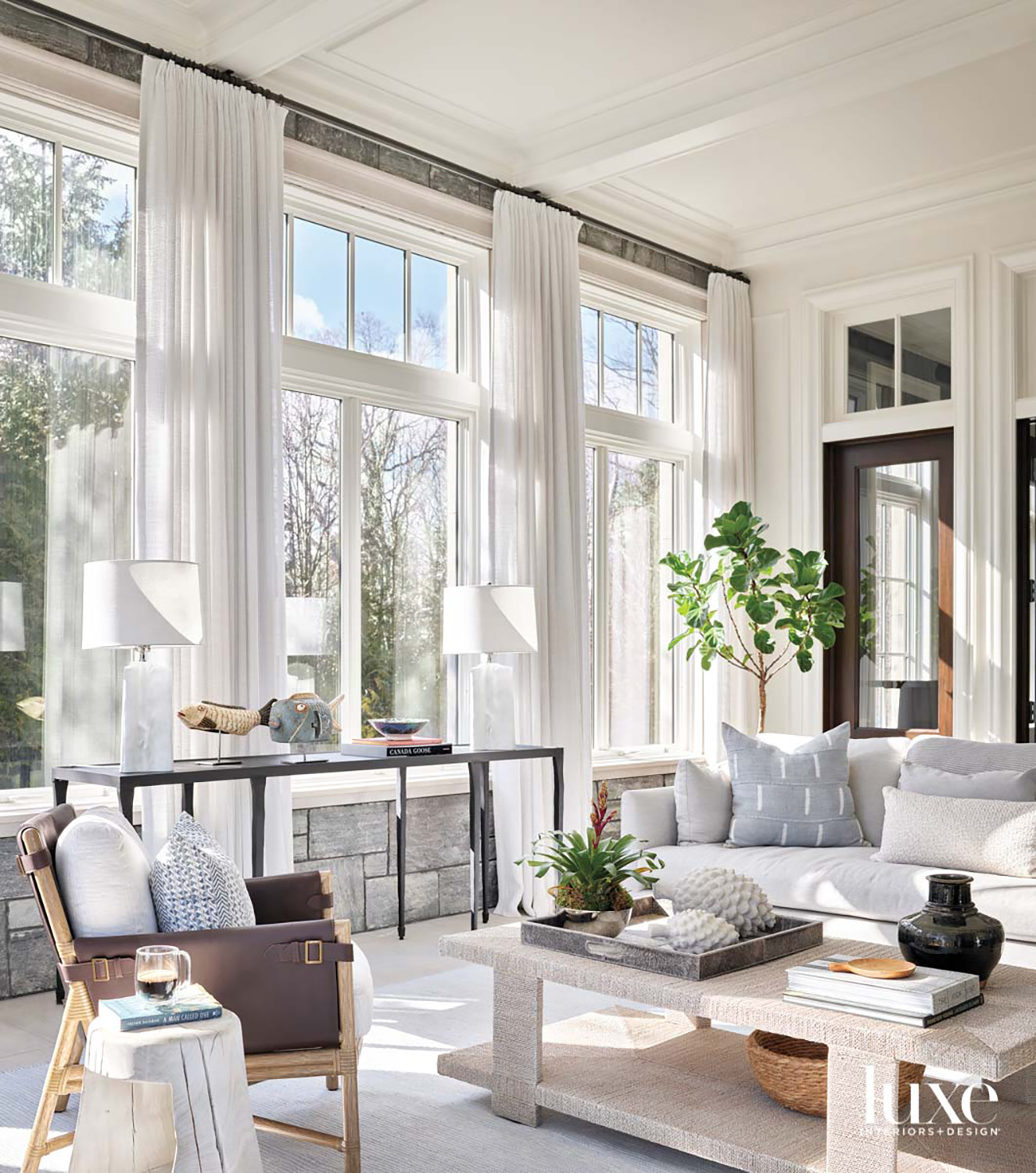 A sunroom with a light gray sofa, a brown leather chair and a textured coffee table.