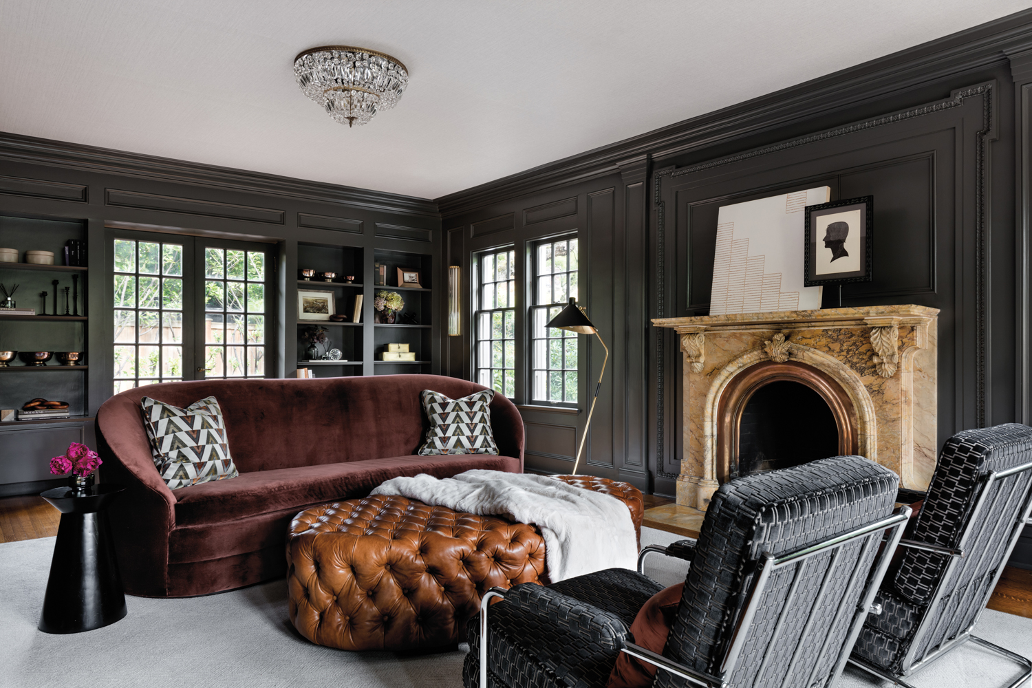 Designed by Shannon Adamson, a gray living room has a berry-colored sofa and a brown leather ottoman