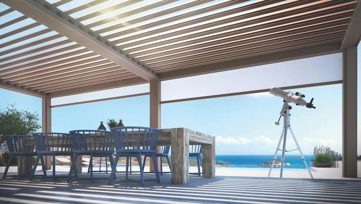 Modern pergola-covered outdoor dining area overlooking the ocean, with a wood table, blue chairs, and a telescope positioned to face the coastal view.
