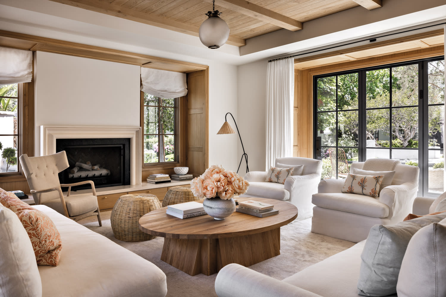 living room with round coffee table topped with flowers, surrounded by two white armchairs, two couches and two woven ottomans