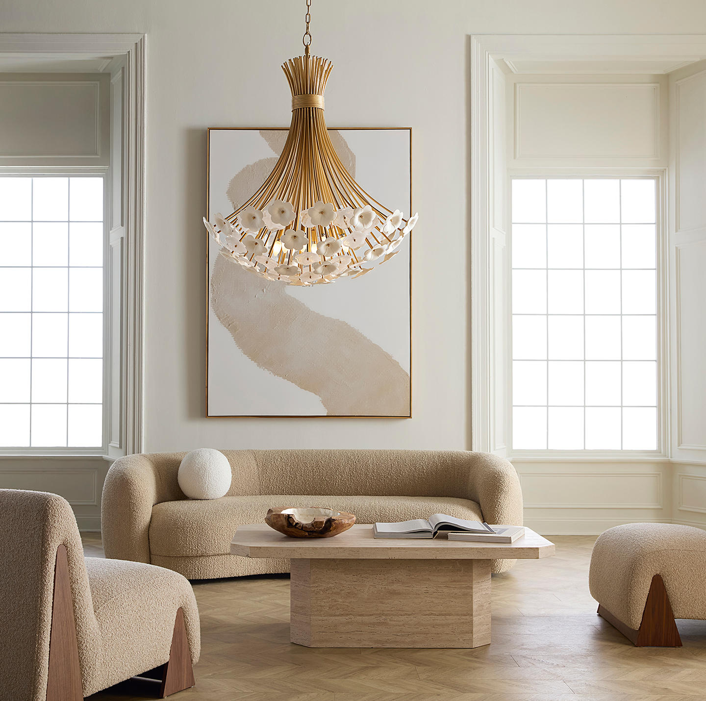 Elegant living room with a beige sofa and armchairs, a wooden coffee table holding a bowl and book, a modern chandelier, and abstract art on the wall.