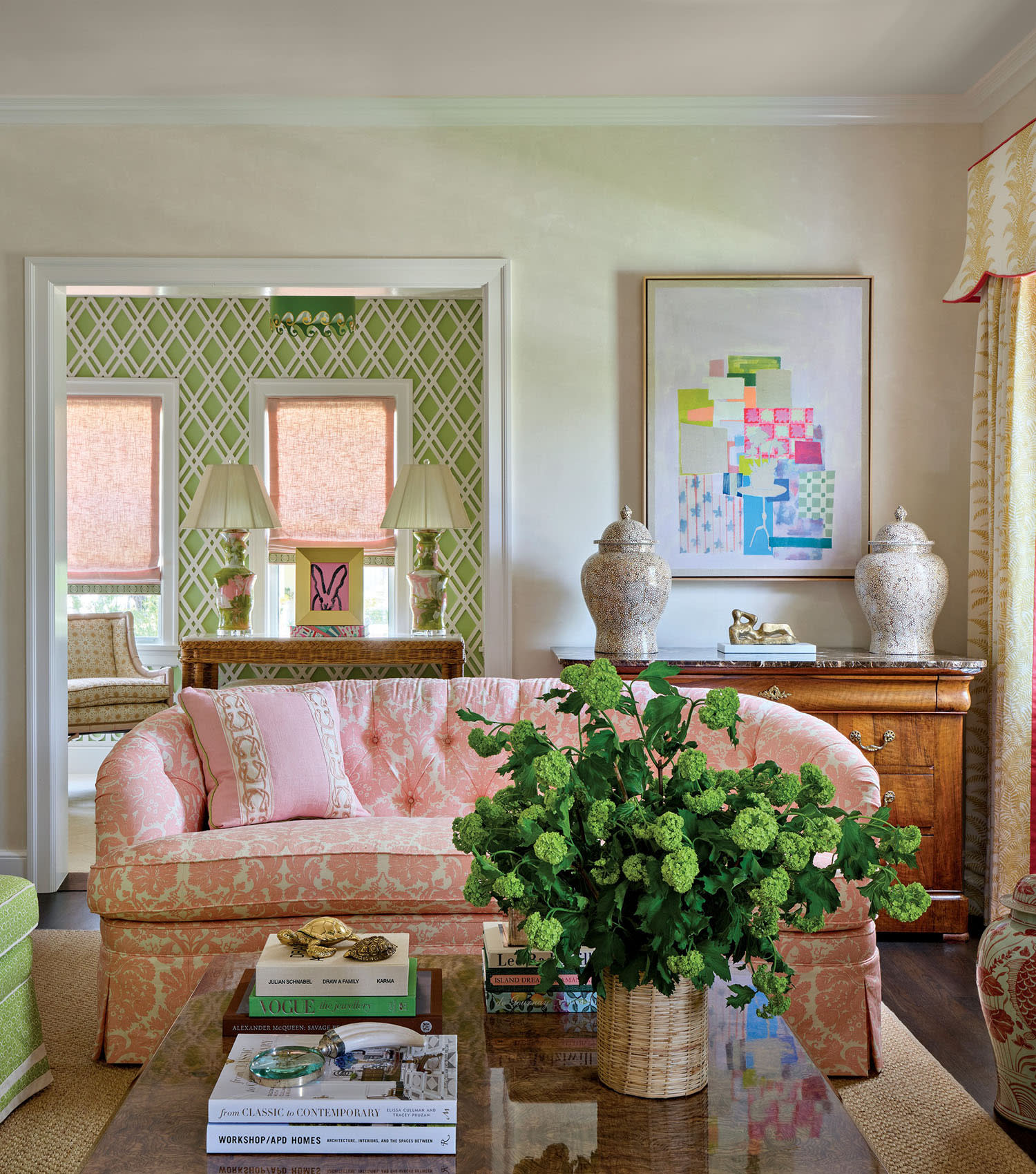 Elegant living room with a pink patterned sofa, green armchair, and glass table holding books and a green bouquet