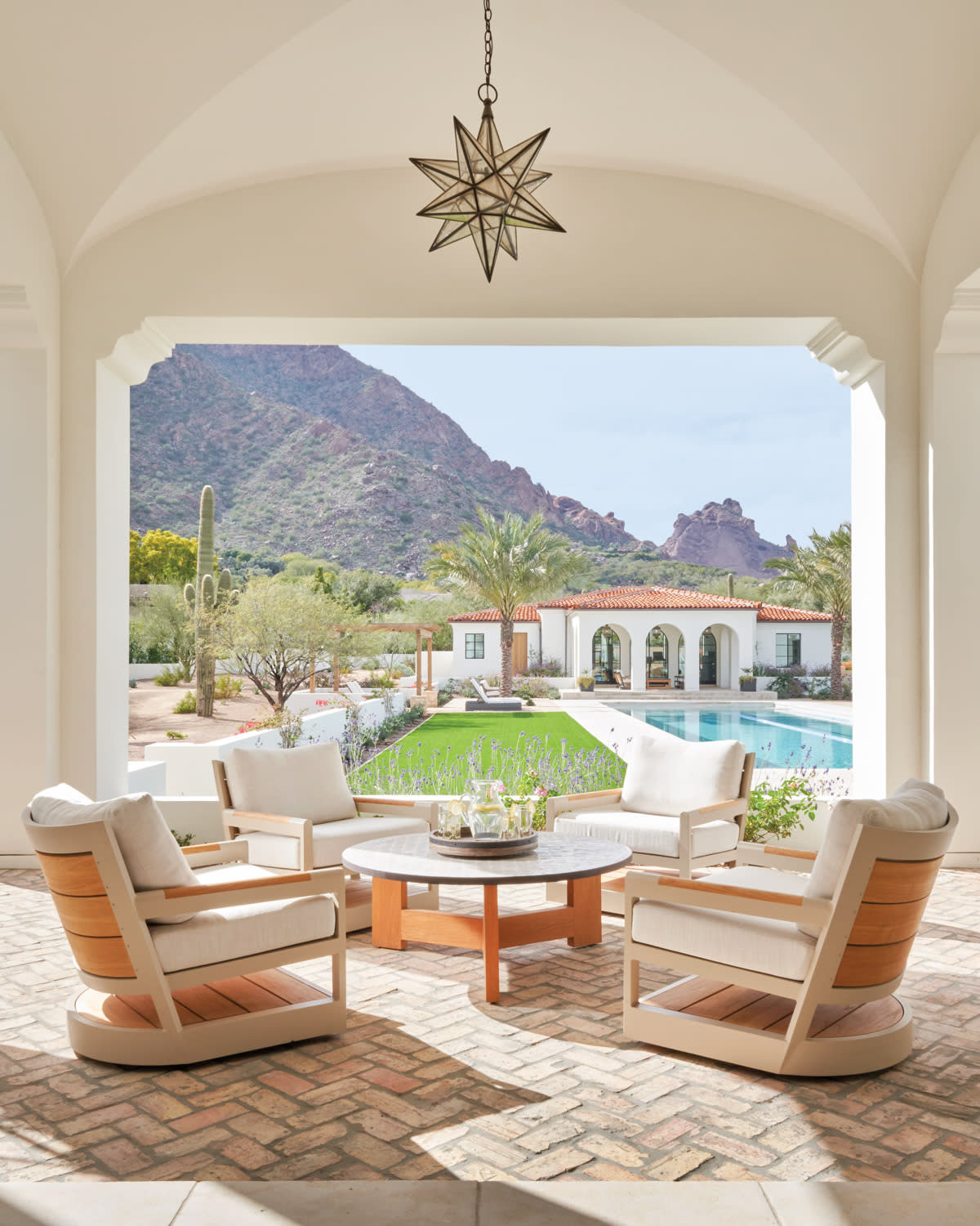 a poolside patio with brick floors and four cushioned armchairs surrounding a teek table