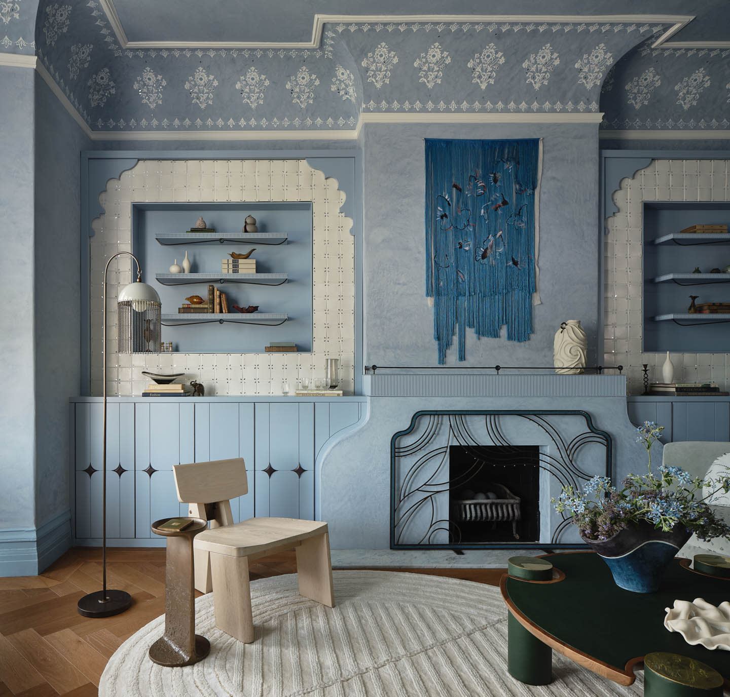 Elegant room with blue patterned walls and ceiling, a wooden chair, a black floor lamp, a textured rug, and decor shelves. A blue wall hanging adds a serene touch.