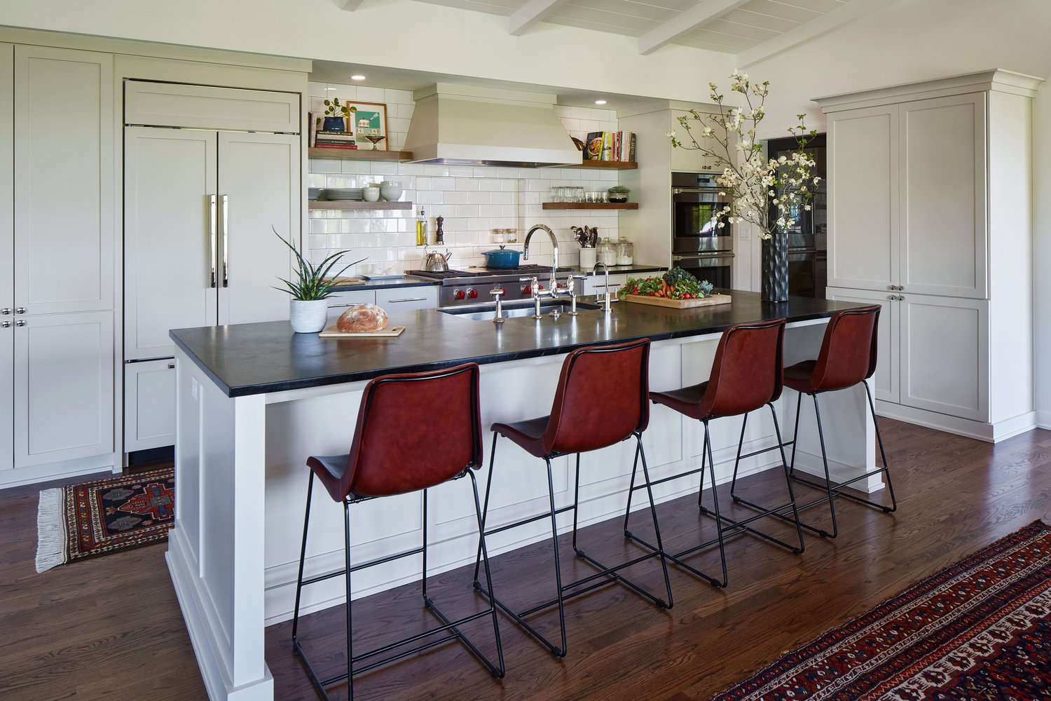 kitchen with white cabinetry and glazed tile backsplash, black countertops and four leather counter stools