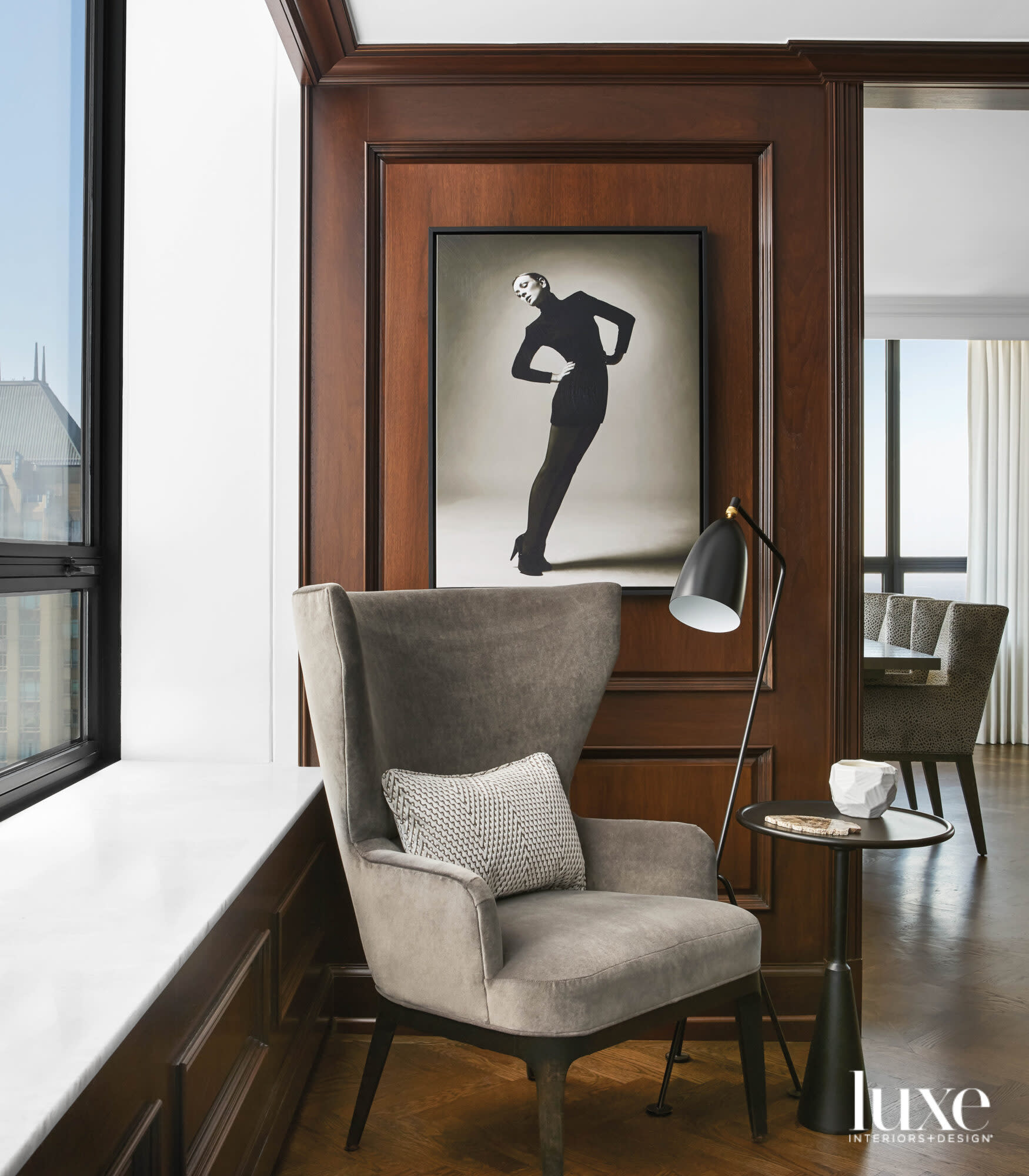 A gray velvet chair sits in front of a black-and-white photograph of a woman.