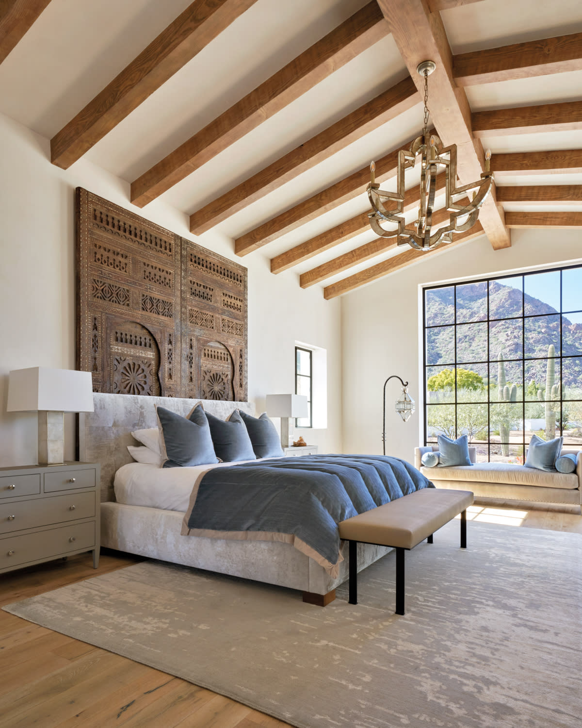 a wood-beamed bedroom with Moroccan doors behind an upholstered bed.