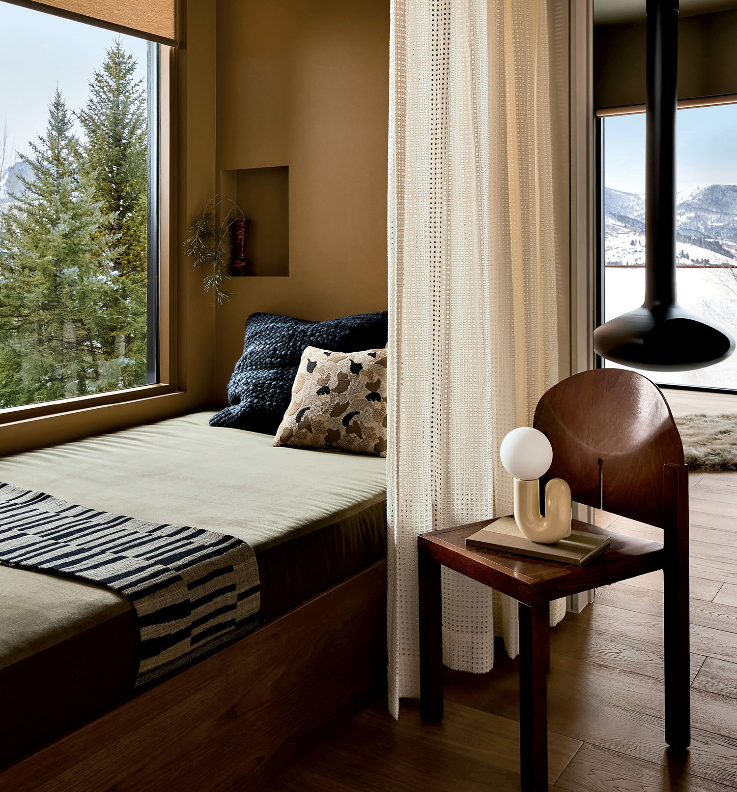 A cushioned bench with pillows in neutral hues with a curtain sitting near a window.