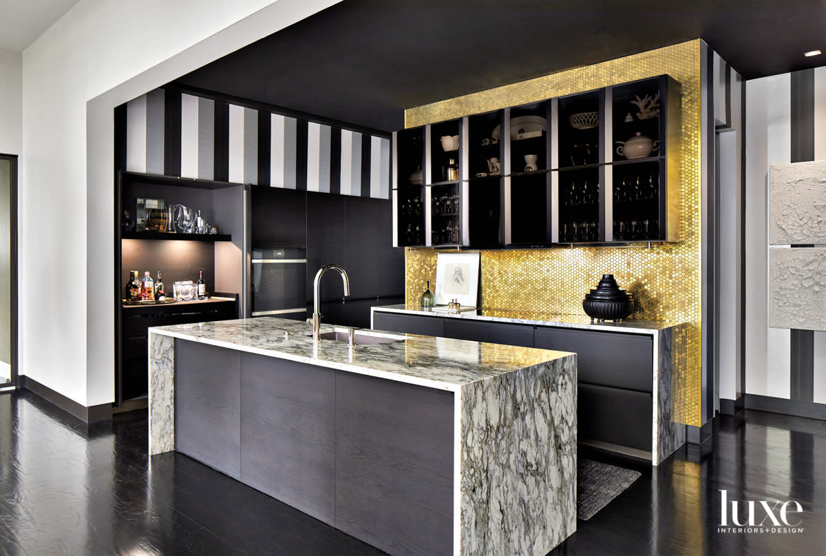 Glamorous kitchen with striped wallpaper accents, gold-toned backsplash tile and a dramatic black-and-white marble island