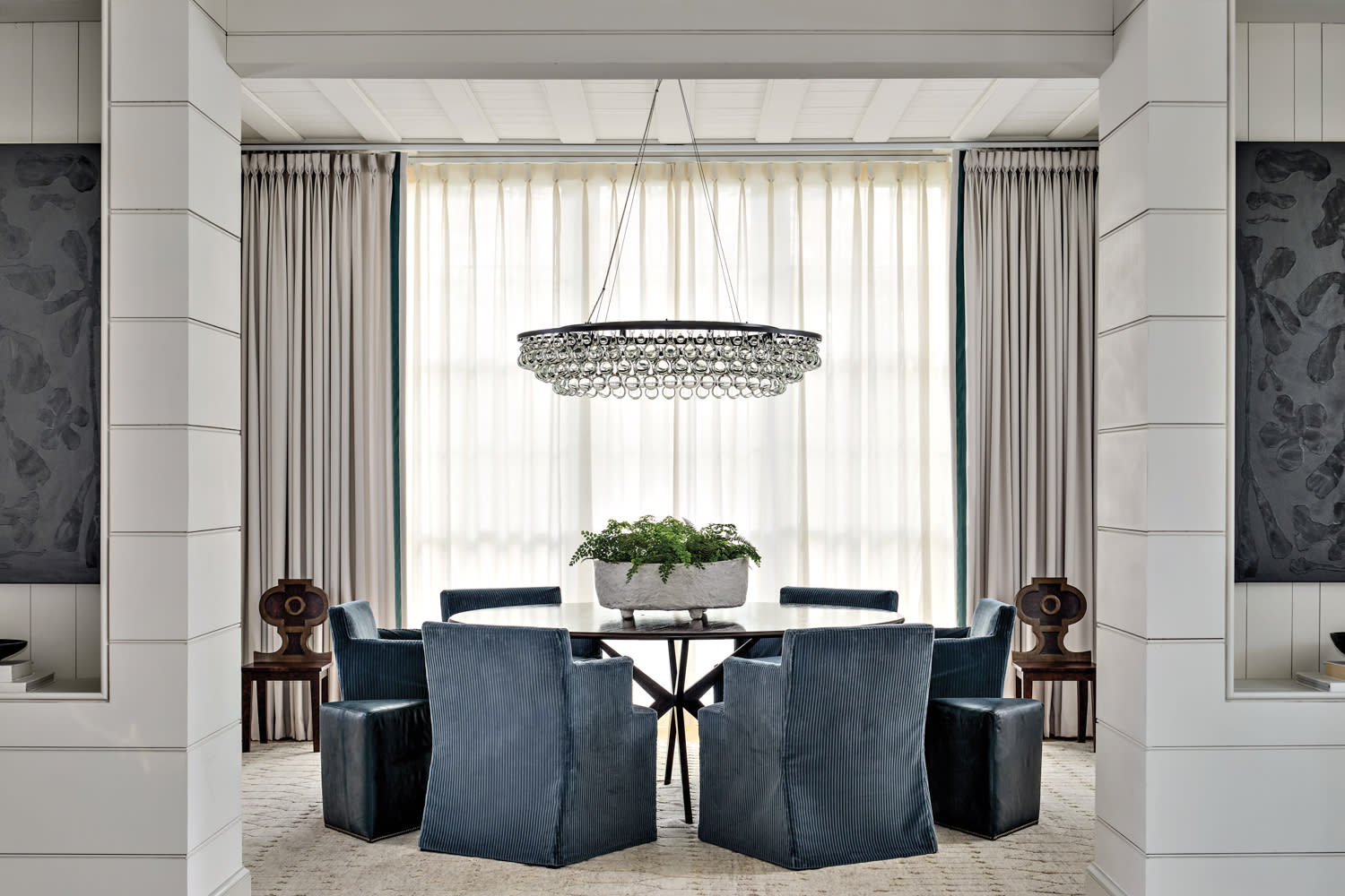 Sophisticated dining room with six blue velvet chairs around a dark wood table, topped with a green centerpiece. A crystal chandelier hangs overhead.