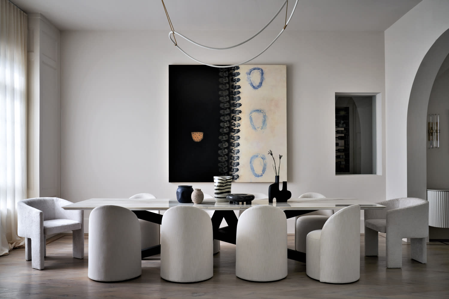 monochrome dining room with an abstract artwork along the wall and a drooping light fixture