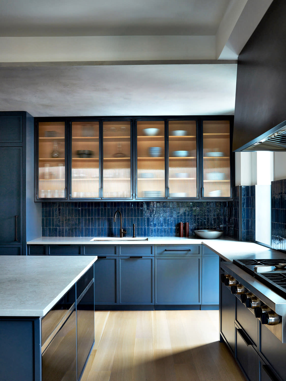 kitchen with warm oak floors and blue cabinetry and matching blue tiles