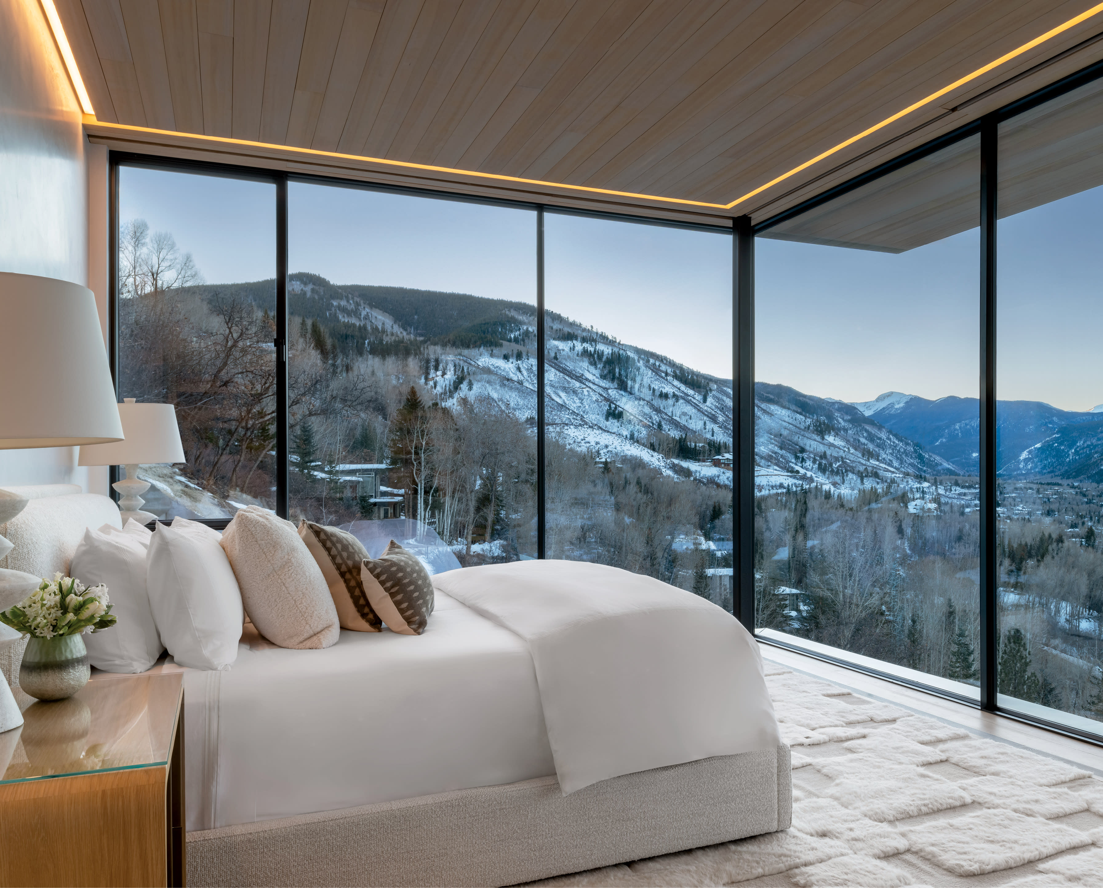 Modern bedroom with floor-to-ceiling windows showcasing a snow-covered mountain view. The room features a plush bed and calming neutral tones.