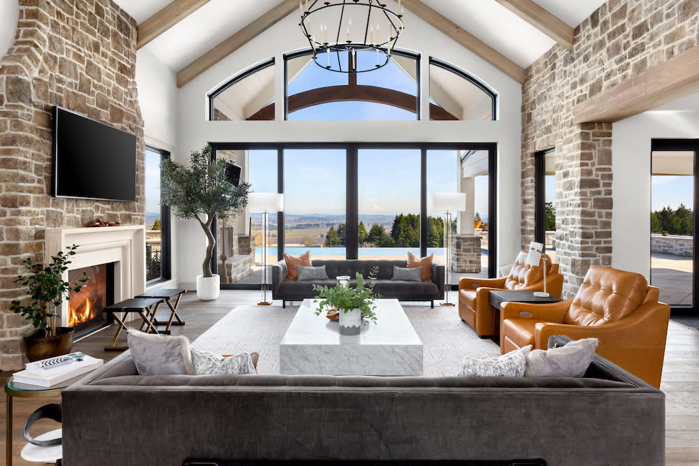 Beautiful living room in new modern luxury home. Features vaulted ceilings, fireplace with roaring fire, and gorgeous exterior view with infinity pool and valley