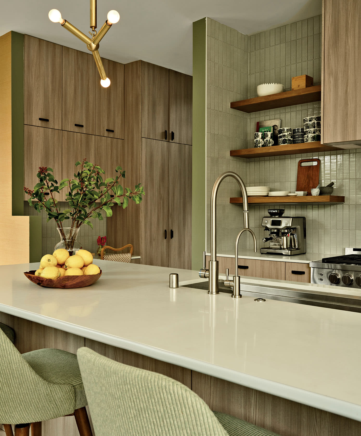 Modern kitchen with light wood cabinets, a white countertop, and green cushioned chairs