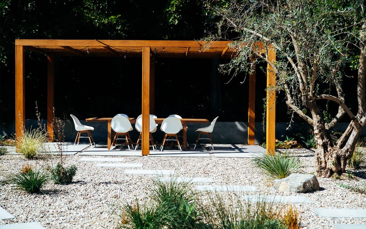 A wooden pergola stands in the center of a gravel area, providing shade and structure to the outdoor space
