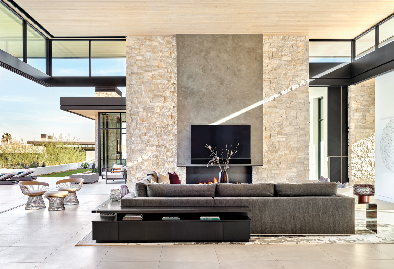 A gray sectional in front of a ceiling-high limestone fireplace. The left side of the room opens up to the outside patio.