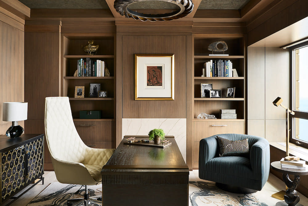 Office with wood paneling and open shelving. Dark wood desk and high back white leather chair.