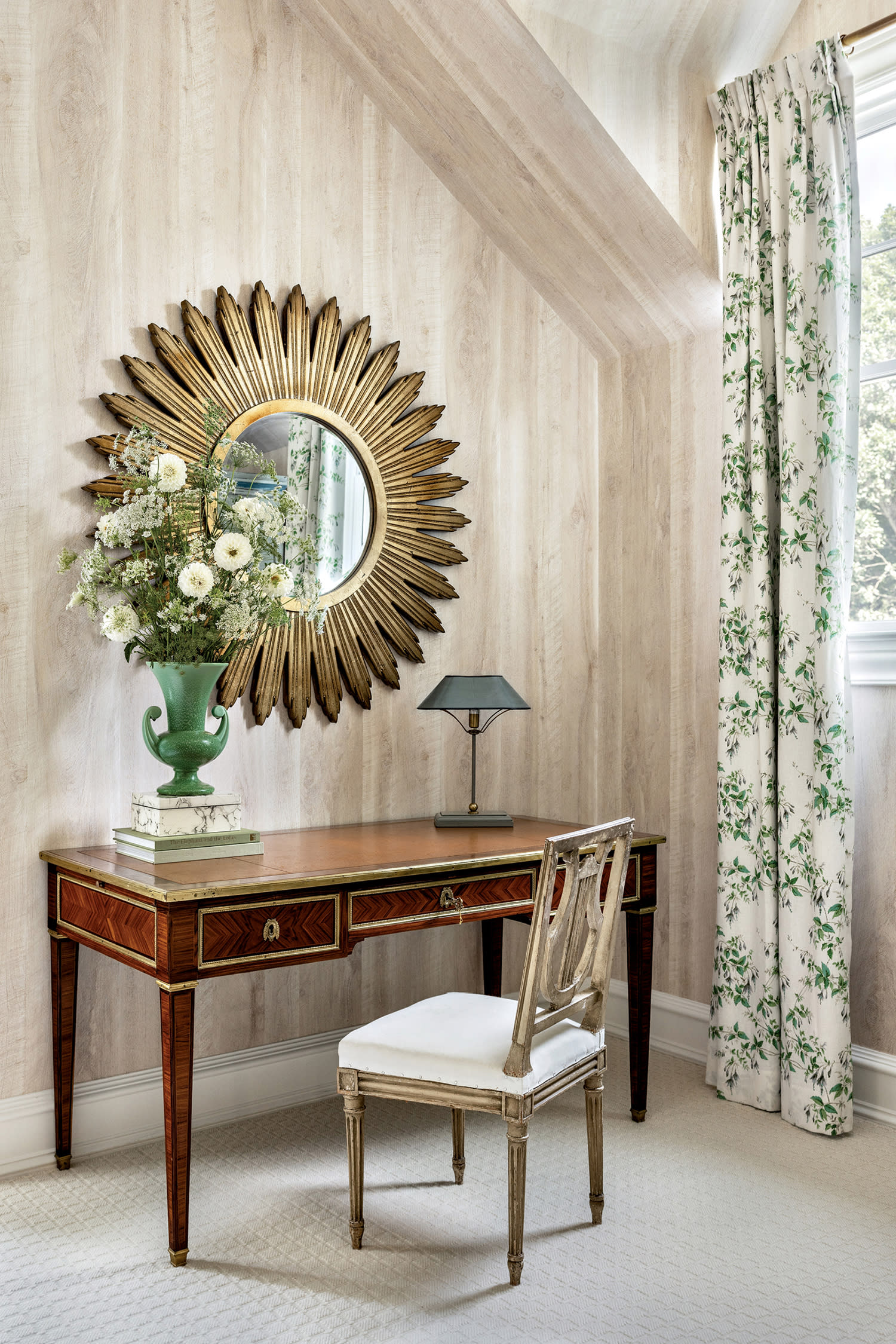 corner of a classic home's bedroom with a vintage desk beneath a sun-shaped mirror