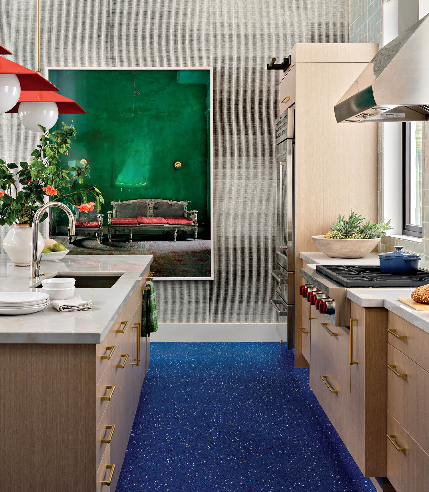 Contemporary kitchen with blue speckled floor, light wood cabinets, and a marble island. Red pendant lights and a vibrant green art piece on the wall.