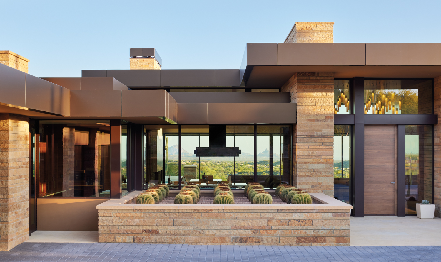 the glass facade of a modern metal-and-stone home with a bed of desert plantings in front