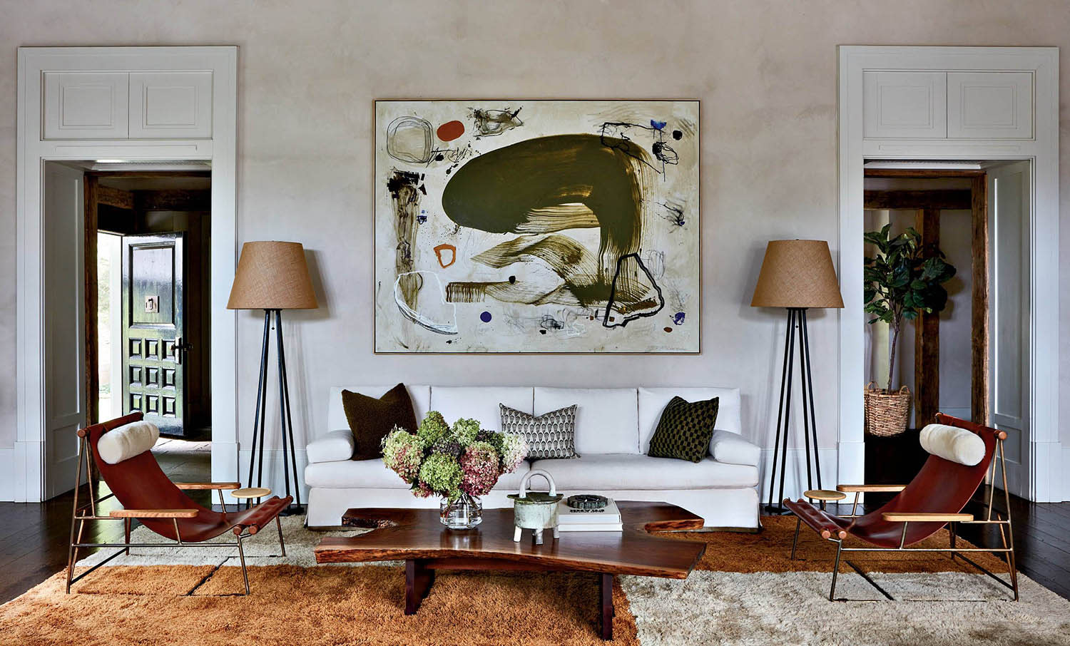 A white couch with accent pillows, floor lamps on either side and a large piece of art on the wall.