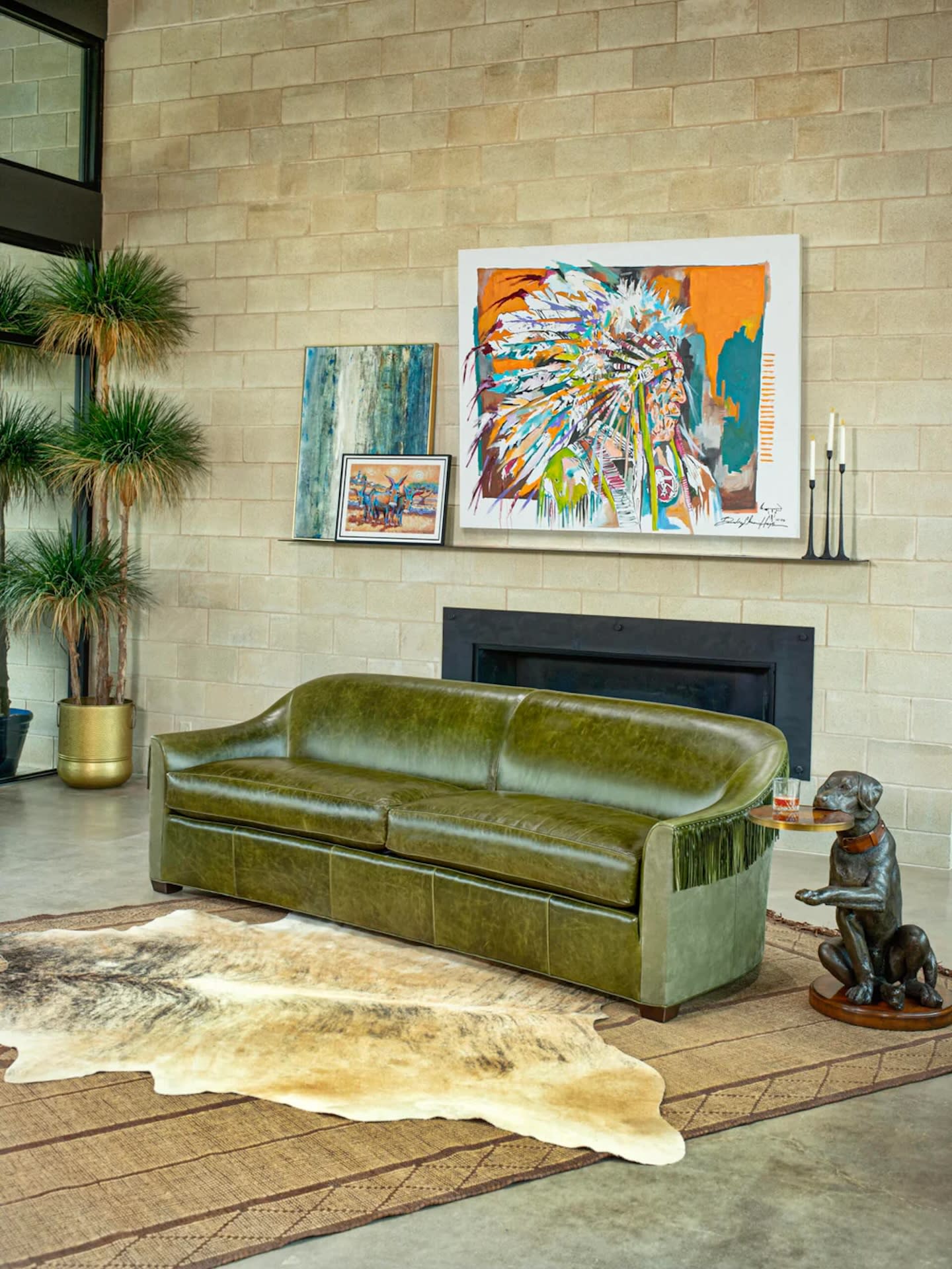 A modern living room with a green leather sofa on a beige and brown patterned rug. Above is colorful art. A plant and sculpture enhance the cozy ambiance.