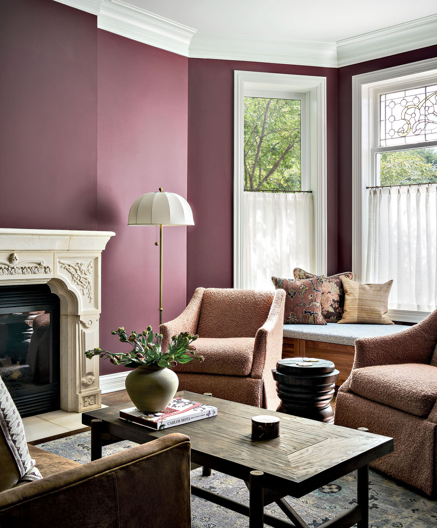A window seat at the back of a pink living room decorated with curtains and a trio of throw pillows.