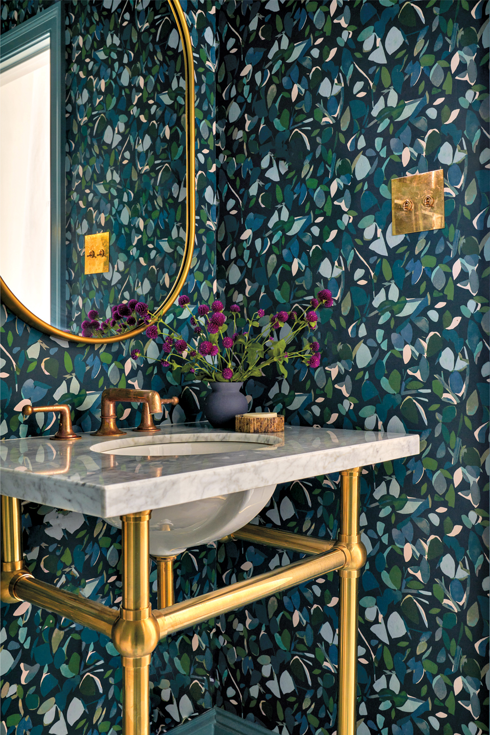 Powder bath with blue-and-green leaf-patterned wallpaper and a brass-accent mirror and sink