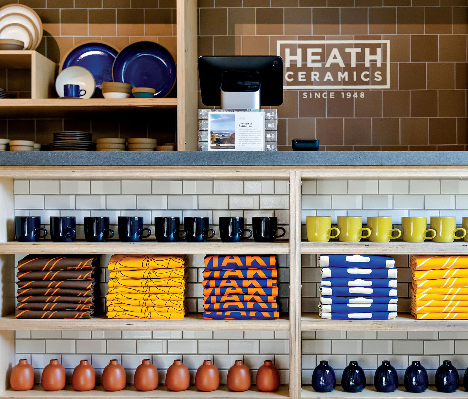 A wall in a showroom with shelves containing ceramic mugs, plates and apparel. 