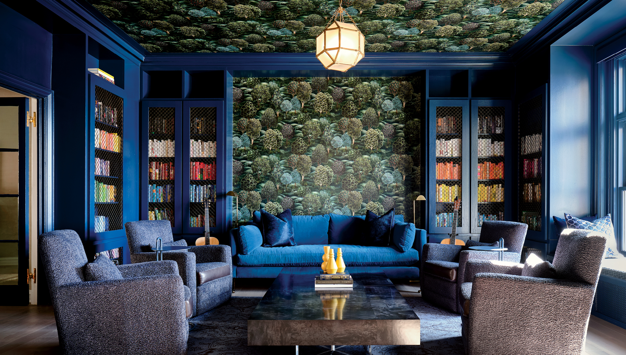 home library with dark blue built-ins and matching seating, along with a forest-inspired wallpaper