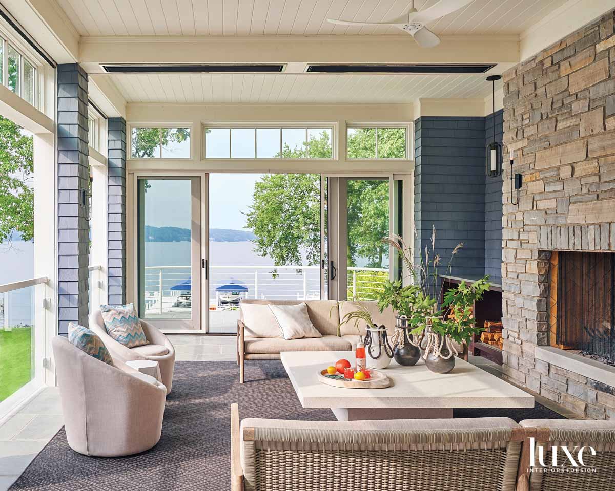 A screened in porch with a stone fireplace. A coffee table is surrounded by two chairs and two sofas.