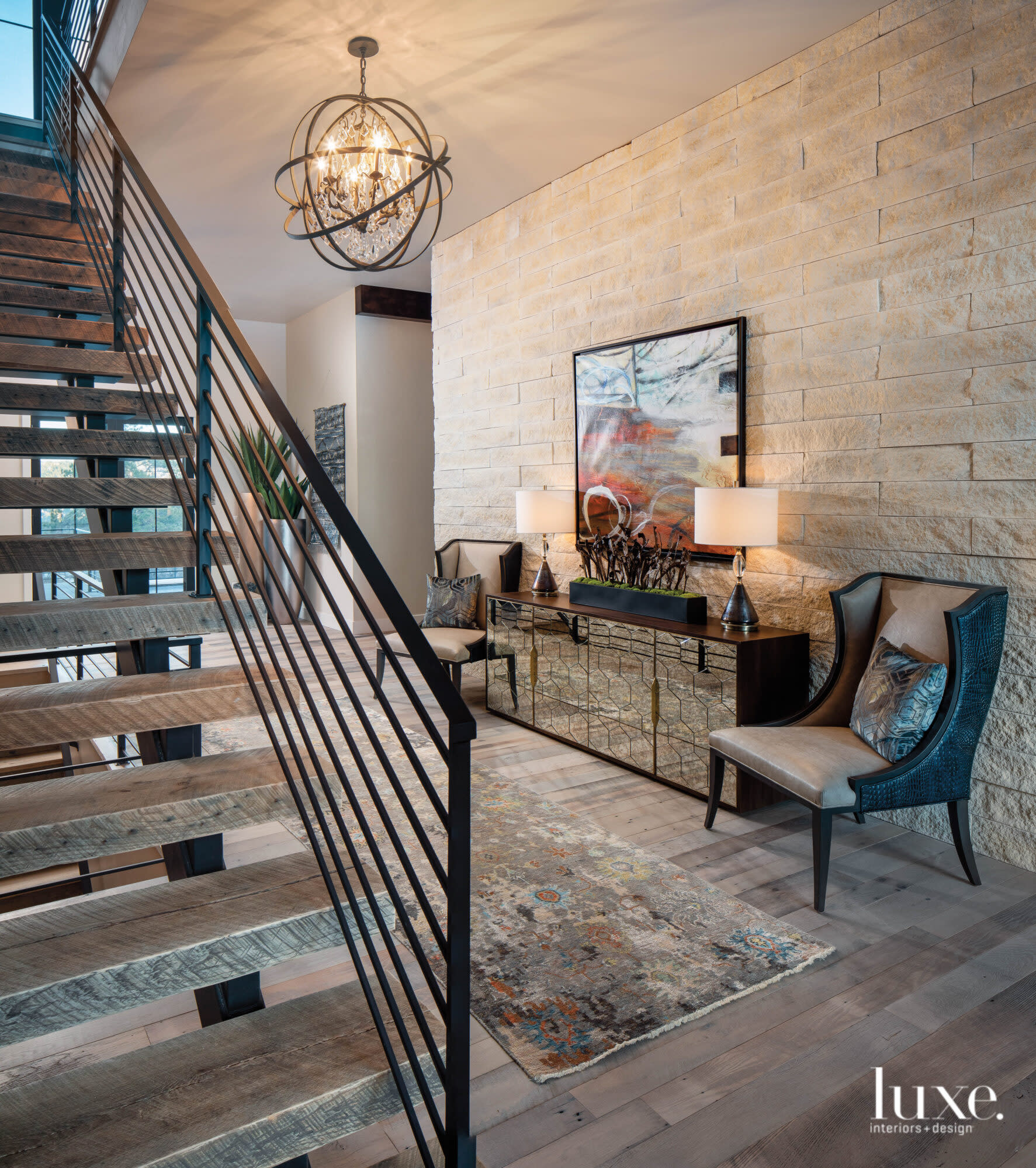An entry has a staircase with a metal rail, two armchairs and artwork.