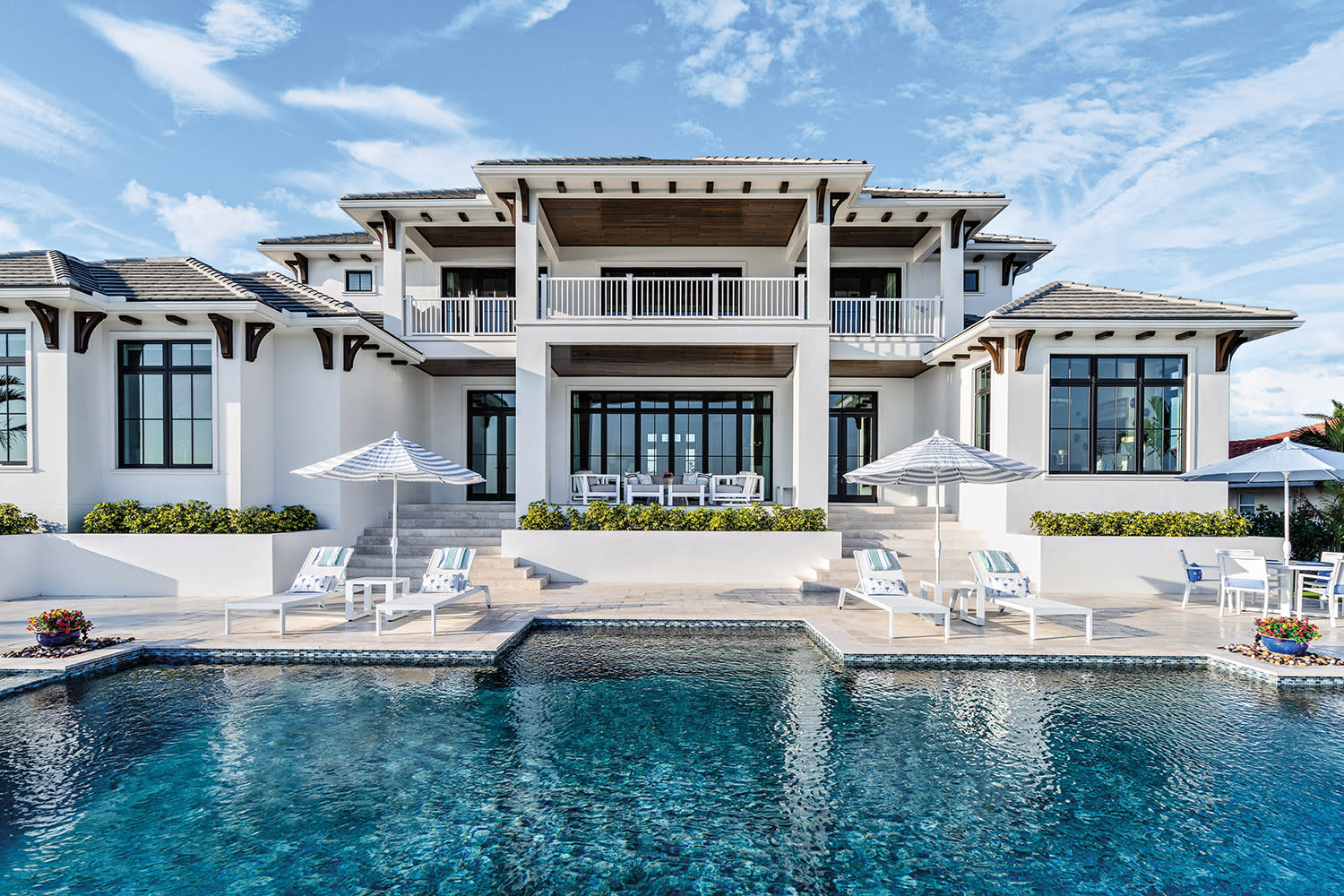 Luxurious modern beachfront home with white facade and a spacious balcony overlooking a pool