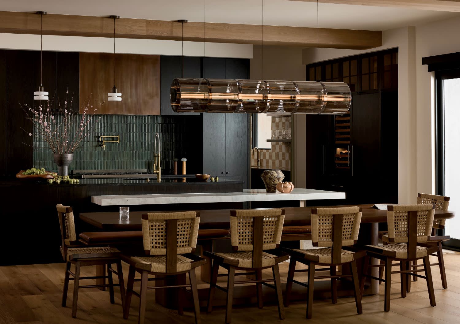 Modern kitchen with dark cabinets, a large wooden dining table, and chairs with woven backs.