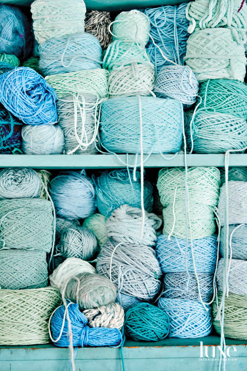 An aqua bookshelf overflowing with spools of yarn in varying shades of aqua