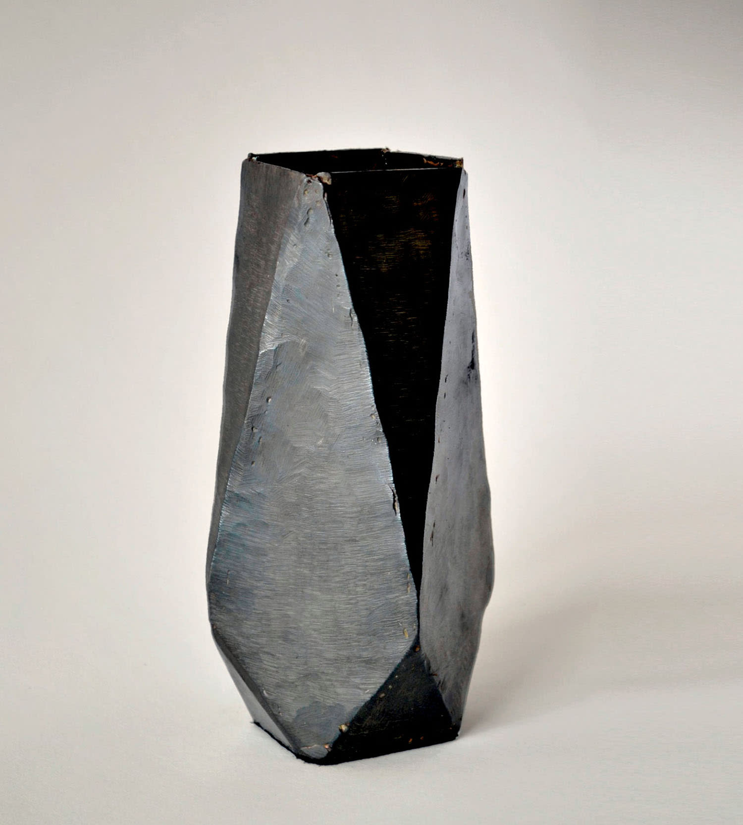 A black stone vase with angular facets on all sides.