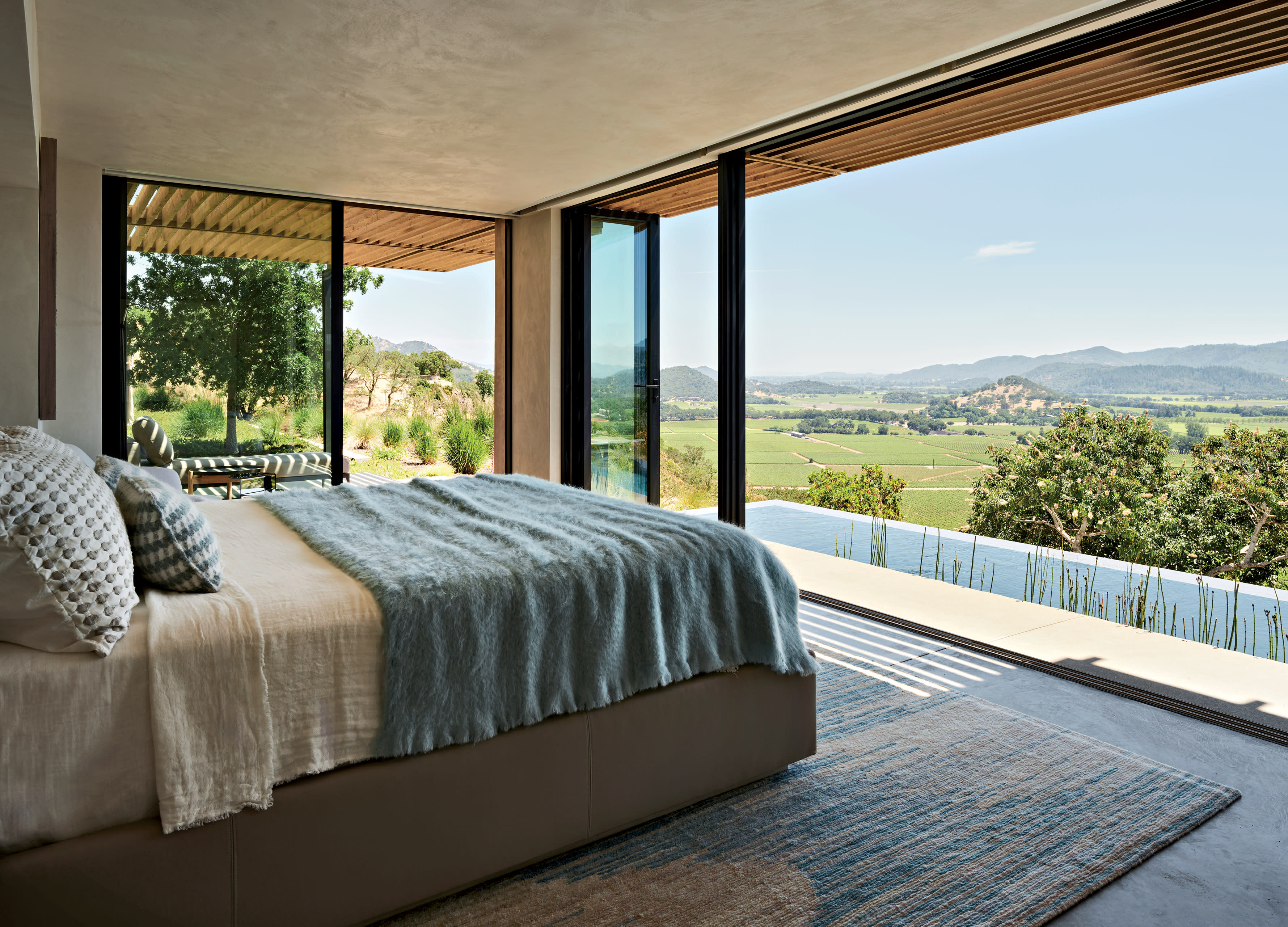 A bedroom with a leather-upholstered bed, blue throw blanket, and accordion doors that open outside.