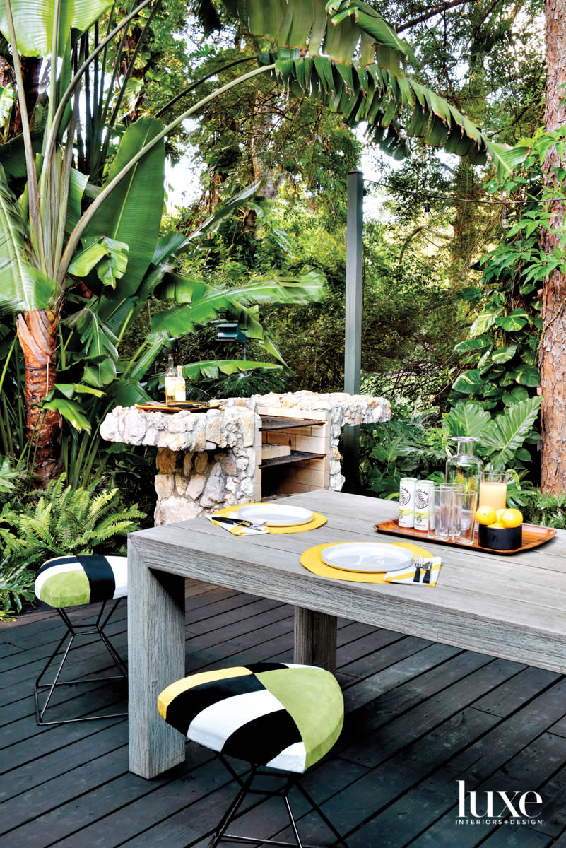 back deck with wood dining table, green stools, brick pizza oven and lush landscaping