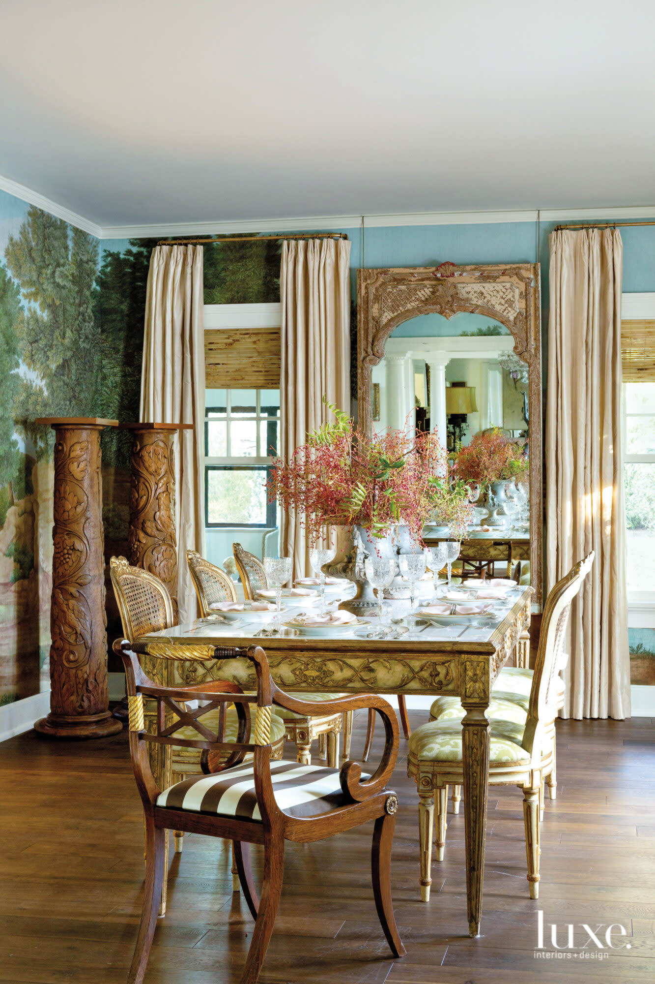 Dining room with scenic wallpaper, tall mirror and pair of carved pedestals