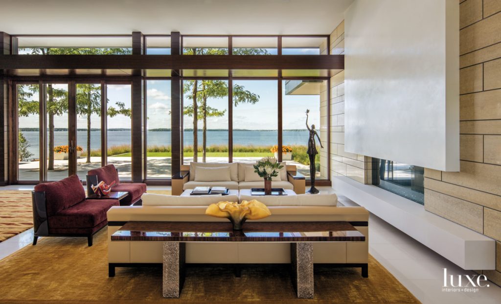 In the light-filled great room, matching sofas and a pair of chairs surround an upholstered cocktail table, all by Liaigre from David Sutherland showroom, in front of a double-faced fireplace made of stone and hand-troweled plaster.