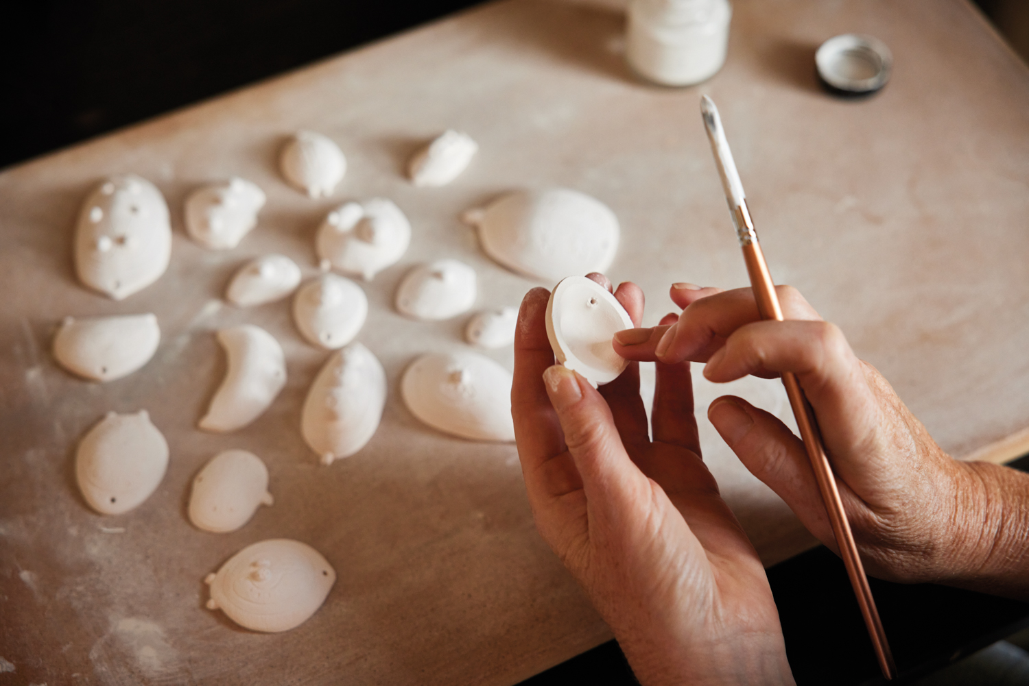 Hands holding a paintbrush and a small porcelain carving.