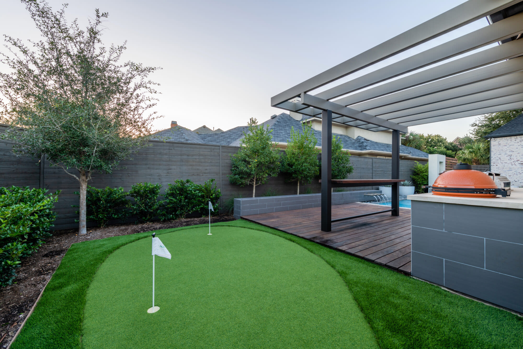 Backyard putting green with pergola-covered deck and grill

